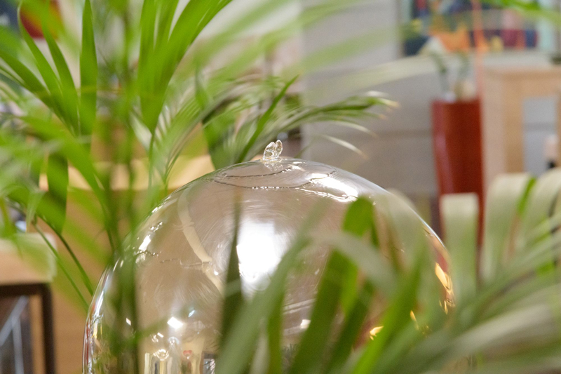 Close-up of the qSkills stainless steel garden fountain in spherical shape with water and green plants.