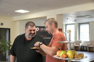 Zwei männliche Teilnehmer im qSkills Cafe & Loungebereich, vorm Obstkorb pausierend, beim Kekse essen.