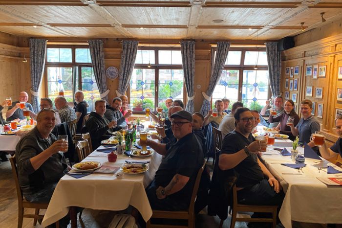 Eine große Gruppe Teilnehmende beim traditionellen qSkills Teilnehmerabend (Montag) im Restaurant "Bratwurst Röslein" beim Abendessen mit gehobenen Gläsern, in ausgelassener Stimmung, sich gegenseitig zuprostend mit Bier.