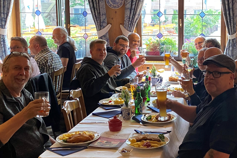 A group of male participants at the traditional qSkills participants' evening (Monday) at the restaurant “Bratwurst Röslein” having dinner, raising their glasses in a lively atmosphere, toasting each other with beer.