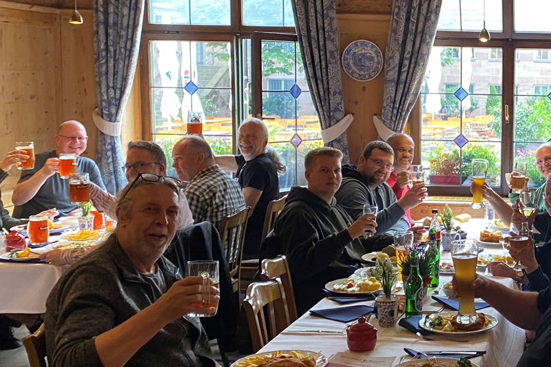 A group of male participants at the traditional qSkills participants' evening (Monday) at the restaurant “Bratwurst Röslein” having dinner, raising their glasses in a lively atmosphere, toasting each other with beer.