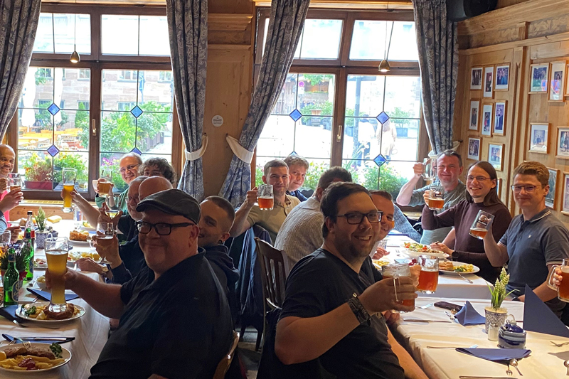 A group of male participants at the traditional qSkills participants' evening (Monday) at the restaurant “Bratwurst Röslein” having dinner, raising their glasses in a lively atmosphere, toasting each other with beer.