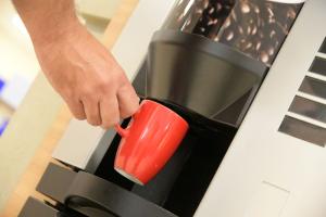 Handrücken eines männlichen Teilnehmers, der am qSkills Kaffeeautomaten eine rote qSkills Tasse in den Ausgabebereich platziert.