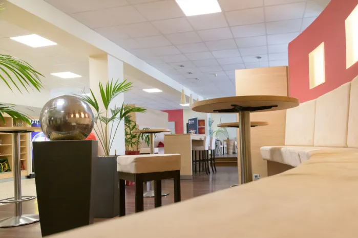 qSkills Cafe & Loungebereich aus der Froschperspektive (von unten nach oben, in den Raum hinein), mit Sitzecke, den Edelstahl-Gartenbrunnen sowie die Stehtische, die Leseecke und die Kaffeeautomaten.