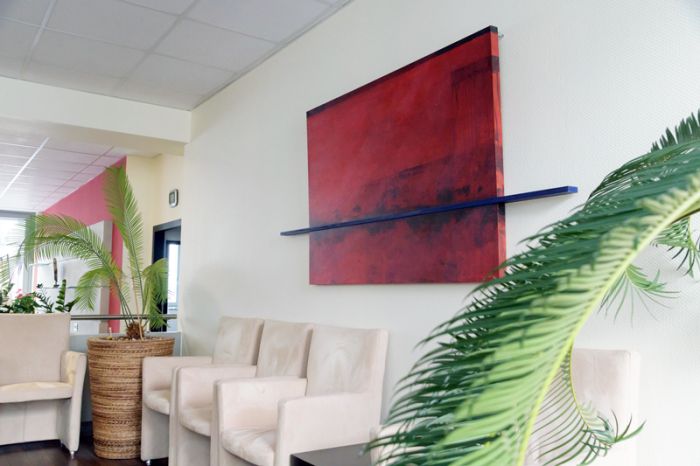 qSkills Lounge mit drei weißer Stühlen, Kübel-Bepflanzung und Wandgemälde mit abstrakter Kunst auf Leinwand in roten und schwarzen Farben.