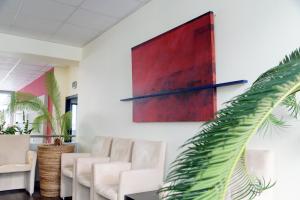 qSkills Lounge mit drei weißer Stühlen, Kübel-Bepflanzung und Wandgemälde mit abstrakter Kunst auf Leinwand in roten und schwarzen Farben.