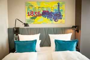 View of a double bed with pillows and duvet cover at the Motel One hotel at Nuremberg Central Station, featuring modern wall art with a railway motif.