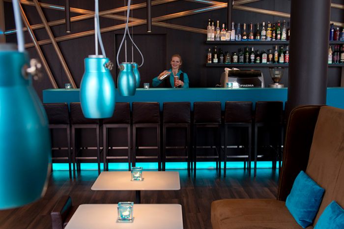 View from the seating area of the bar and the bartender, as well as a variety of bottles at the Motel One Nuremberg-City hotel.