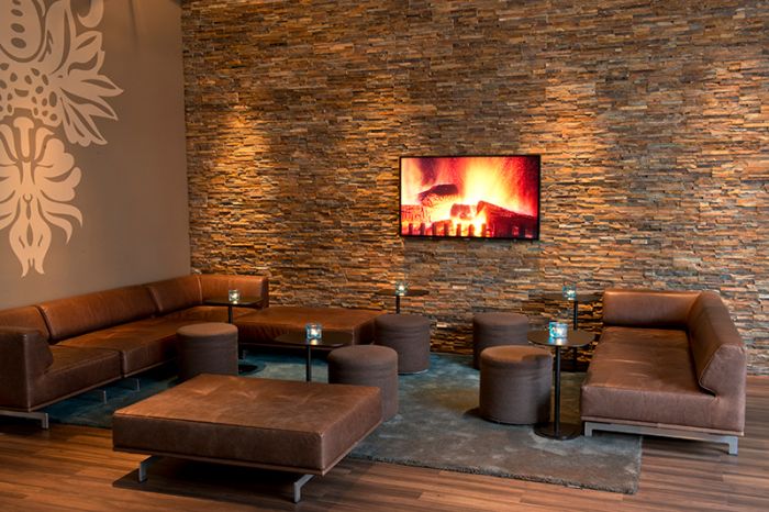 Comfortable seating area with couches for relaxing, featuring design elements such as a stone wall, flat-screen TV, and fireplace at the Motel One Nuremberg-City hotel.