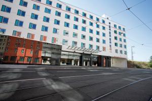Exterior view of the Motel One Nuremberg-City hotel with a view of the main entrance and façade from across the street, including the street view and tram tracks.