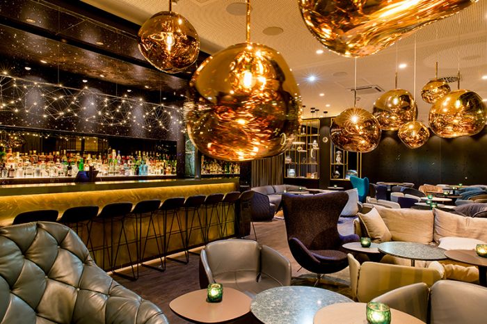 Lounge area overlooking the bar with modern golden spherical ceiling lights at the Motel One Nuremberg-Plärrer hotel.