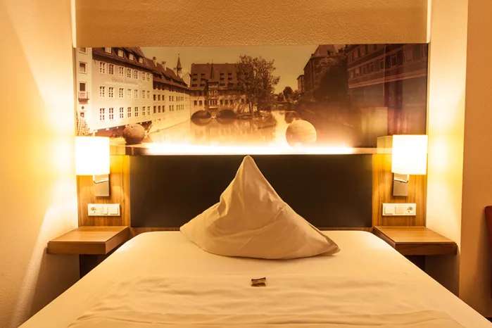Novina Hotel Tillypark Nuremberg: View of single room with bed and mural of the old town with indirect lighting.