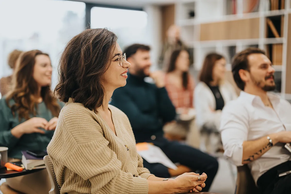 Smiling woman participating in a professional workshop with colleagues in a modern office setting, conveying engagement and teamwork.