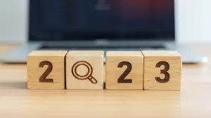 2023 Holzblock mit Lupensymbol vor Laptophintergrund