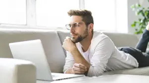 Mann durchsucht seinen Laptop, zu Hause auf dem Sofa