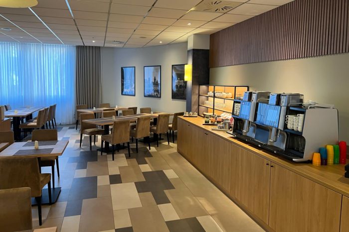 Restaurantbereich im NOVINA Hotel am Südwestpark Nürnberg mit mit Kaffeemaschinen, Fußboden sowie mehreren Tischen mit Stühlen ohne Gäste.