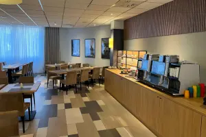Restaurant area in the NOVINA Hotel at Südwestpark Nuremberg with coffee machines, flooring, and several tables with chairs without guests.