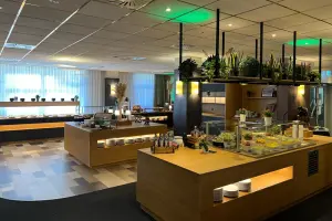 Restaurant area at the NOVINA Hotel at Südwestpark in Nuremberg with salad buffet, food serving area, and dessert area without guests and green ceiling lighting.