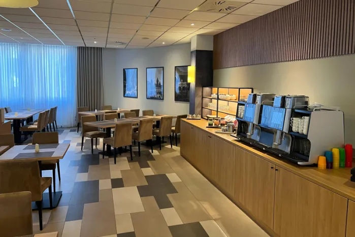 Restaurantbereich im NOVINA Hotel am Südwestpark Nürnberg mit mit Kaffeemaschinen, Fußboden sowie mehreren Tischen mit Stühlen ohne Gäste.